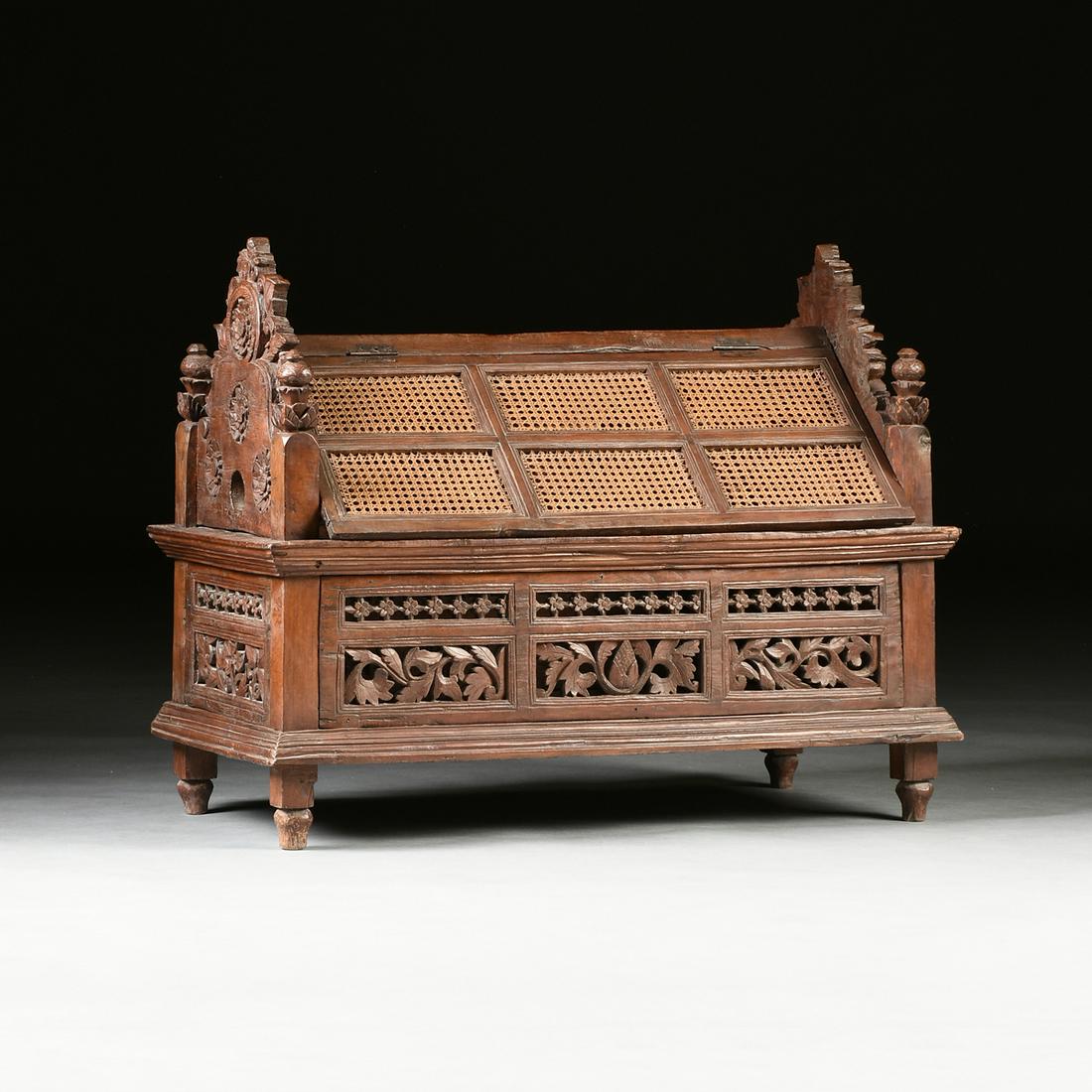 AN ANGLO INDIAN CANED AND CARVED HARDWOOD CHEST,: AN ANGLO INDIAN CANED AND CARVED HARDWOOD CHEST, POSSIBLY SOUTHEAST ASIAN, 19TH CENTURY, in a pseudo Dutch Renaissance architecture style with a hinged cane paneled peaked roof top opening to a simple