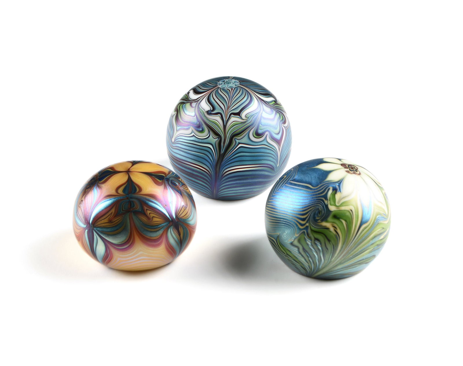 THREE ORIENT AND FLUME IRIDESCENT ART GLASS: THREE ORIENT AND FLUME IRIDESCENT ART GLASS PAPERWEIGHTS, CALIFORNIA, 1975-1979, comprising a yellow ground paperweight with four iridescent pulled flowers, 1975; a blue ground paperweight with white 