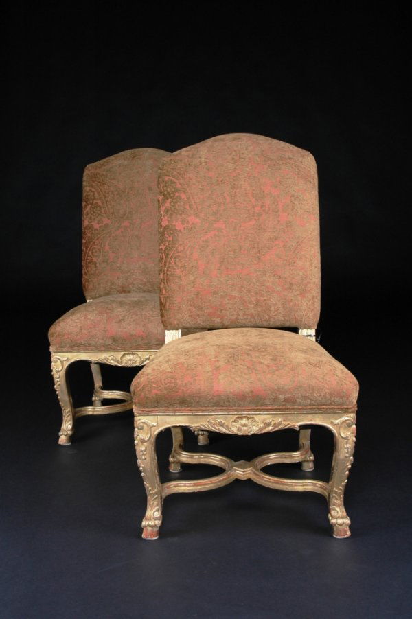 A PAIR OF RÉGENCE GILTWOOD CHAISES, each with arch: A PAIR OF RÉGENCE GILTWOOD CHAISES, each with arched padded backrest on fluted supports above a trapezoidal seat with a serpentine seat rail centering a carved shell issuing stylized leaves flanked b