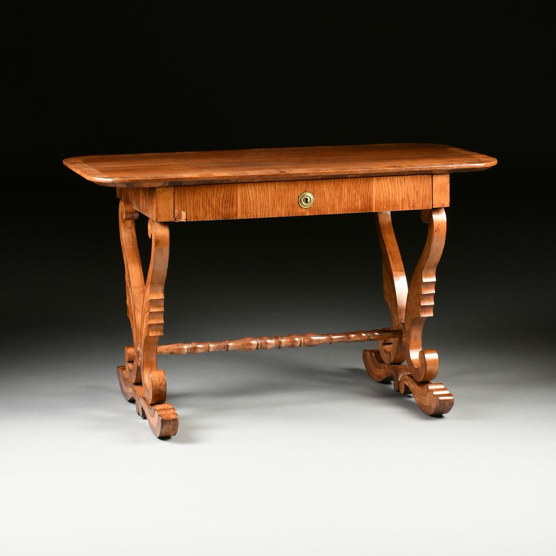A BIEDERMEIER CARVED FRUITWOOD WRITING DESK, AUSTRIAN,: A BIEDERMEIER CARVED FRUITWOOD WRITING DESK, AUSTRIAN, 1820s, the rectangular top above a single drawer frieze centering a gilt brass disc form beaded escutcheon, raised on paired scrolling "S" form l