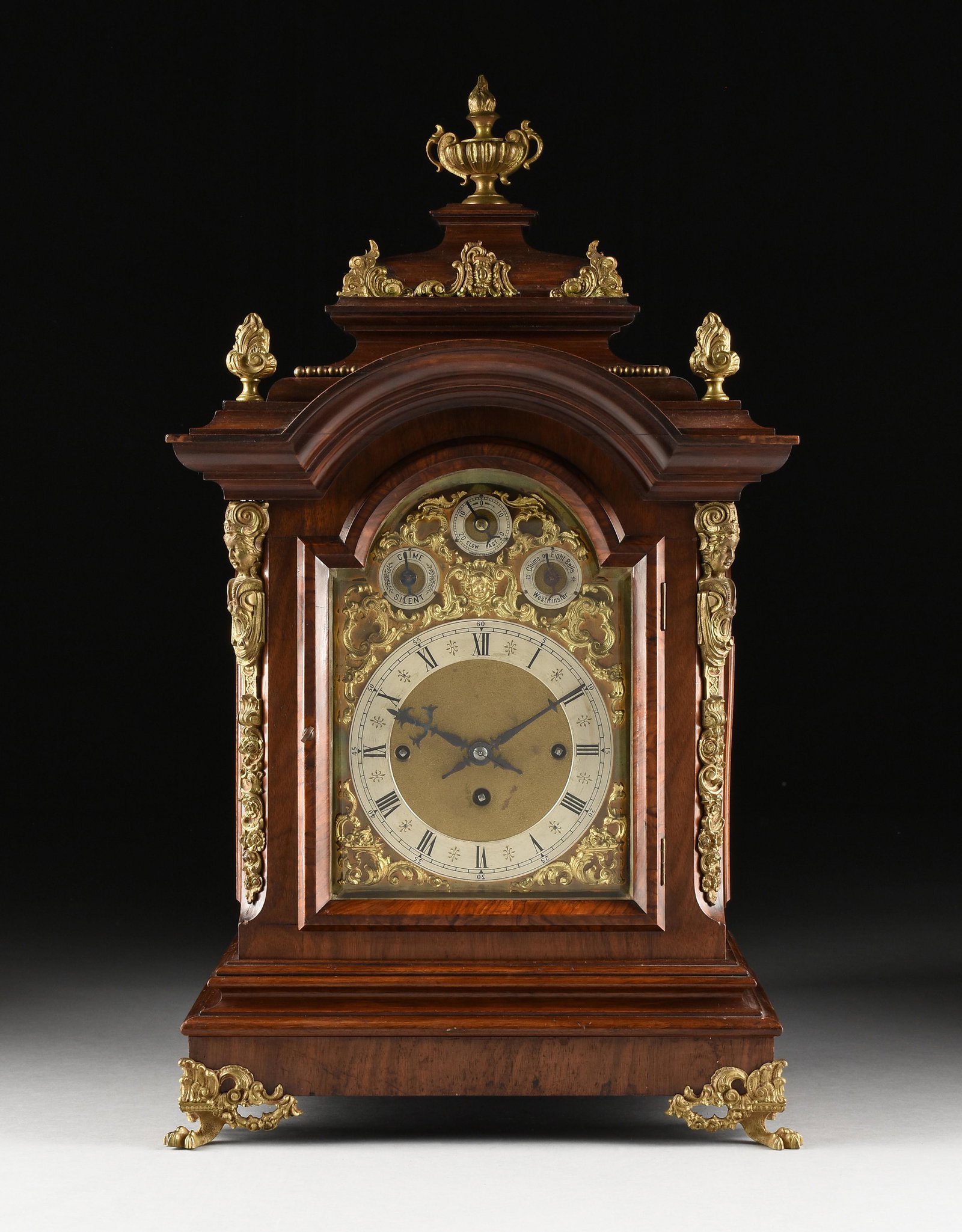 A GERMAN GILT BRASS MOUNTED WALNUT STRIKING BRACKET: A GERMAN GILT BRASS MOUNTED WALNUT STRIKING BRACKET CLOCK, 20TH CENTURY, the step molded cornice surmounted by a two-handled flaming urn above a "C" scrolled cartouche mount within similarly modeled d