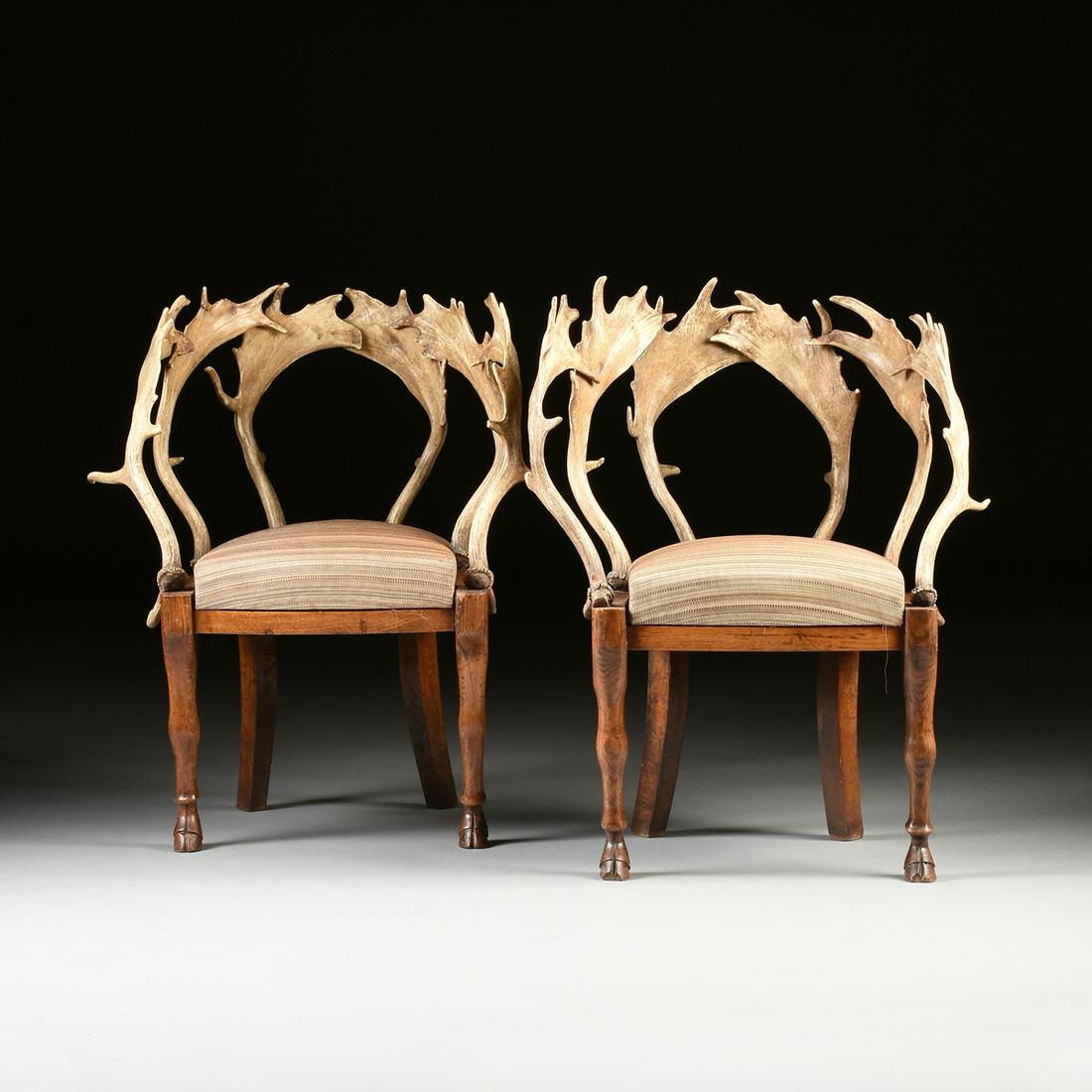 A PAIR OF BIEDERMEIER ANTLER AND CARVED ELM CHAIRS,: A PAIR OF BIEDERMEIER ANTLER AND CARVED ELM CHAIRS, POSSIBLY GERMAN, EARLY 19TH CENTURY, each with curved antler rack backs on a demi-lune seat with drop-in seat cushion, above a flat frieze and raise