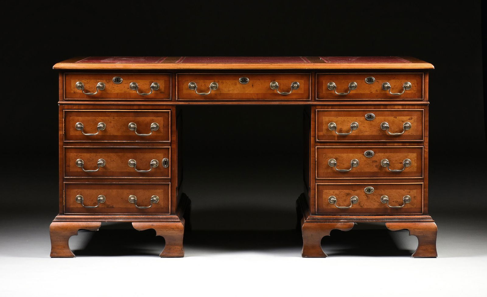 A GEORGE II STYLE WALNUT BURGUNDY LEATHER TOP PARTNER'S: A GEORGE II STYLE WALNUT BURGUNDY LEATHER TOP PARTNER'S DESK, ENGLISH, MID 20TH CENTURY, modeled after Library Tables by Thomas Chippendale (1718-1779), the rectangular burl walnut top with three inse