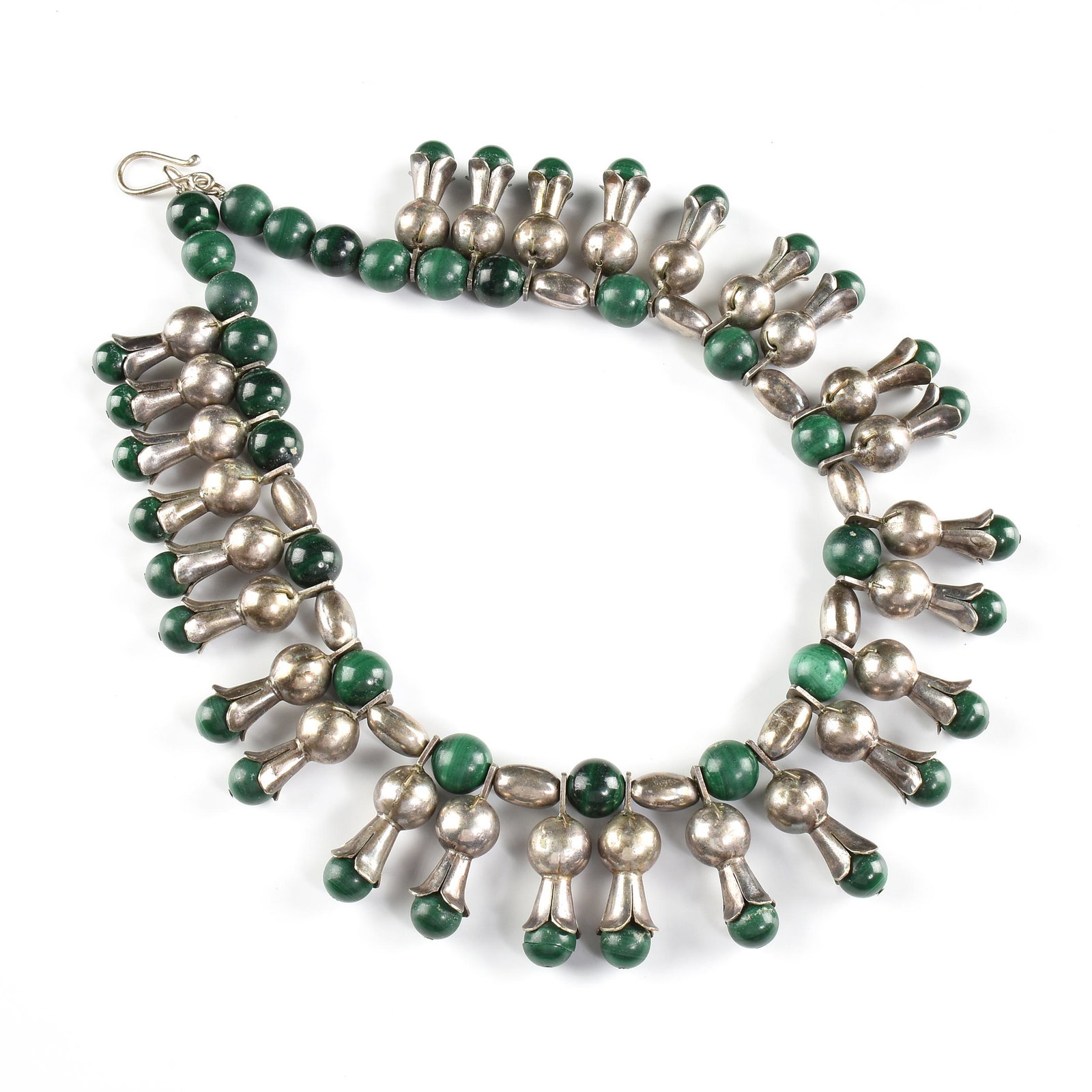 A NAVAJO STYLE TRIBAL SILVER AND MALACHITE SQUASH: A NAVAJO STYLE TRIBAL SILVER AND MALACHITE SQUASH BLOSSOM NECKLACE, 20TH CENTURY, round malachite beads and silver pill form beads intersperse trumpet blooms, enclosing with a hook clasp, length: 9". 