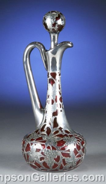 AN AMERICAN SILVER OVERLAY RUBY GLASS DECANTER AND: AN AMERICAN SILVER OVERLAY RUBY GLASS DECANTER AND STOPPER, first quarter 20th century, the ruby glass covered with sterling cage of scrolling leaf and grape motifs, inserted with conforming stopper.