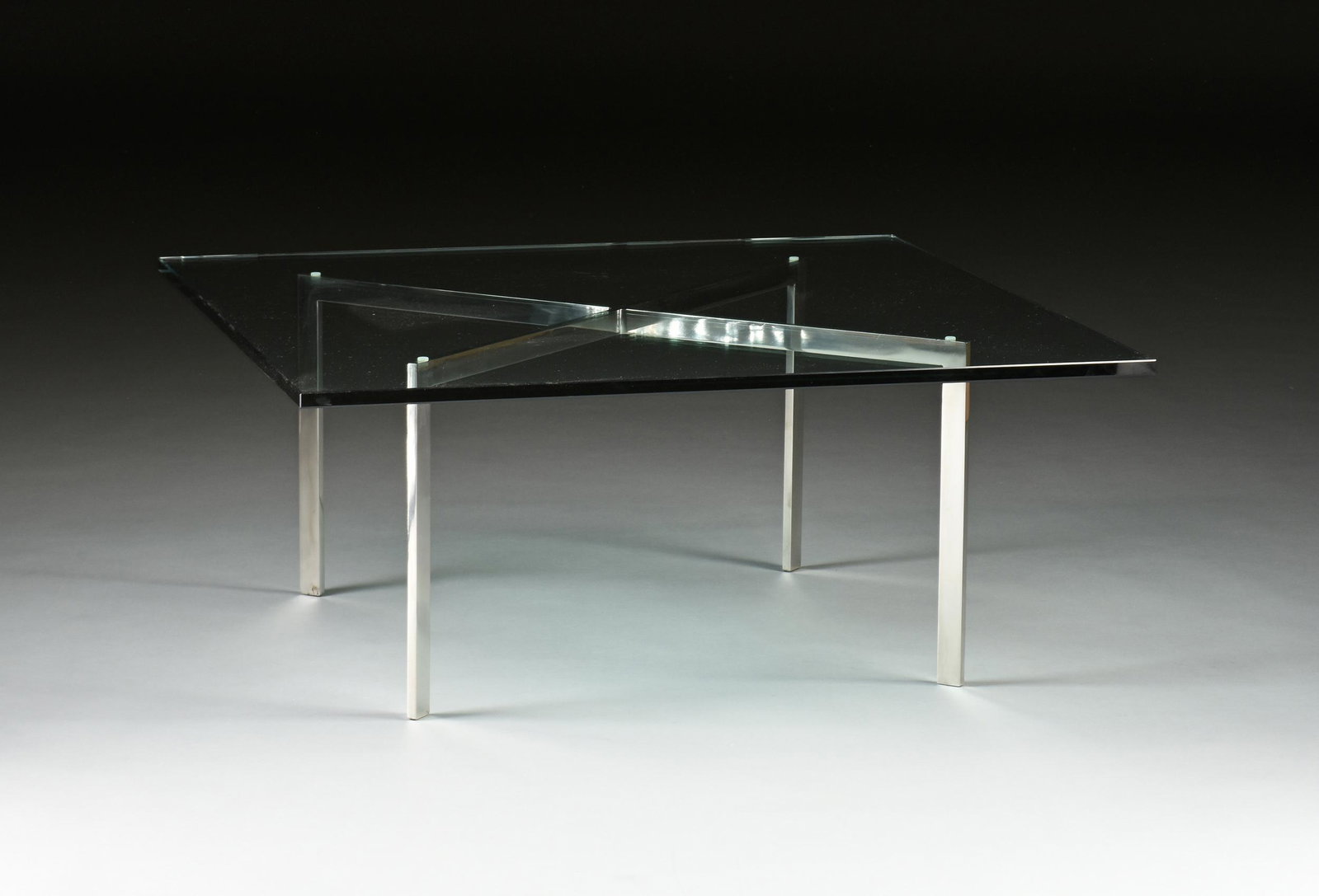 A "BARCELONA" COFFEE TABLE, after DESIGNS BY LUDWIG: A "BARCELONA" COFFEE TABLE, after DESIGNS BY LUDWIG MIES VAN DER ROHE AND LILLY REICH, MID/LATE 20TH CENTURY, the 3/4" thick beveled glass square top on a chrome base, engraved number "333" at base. H