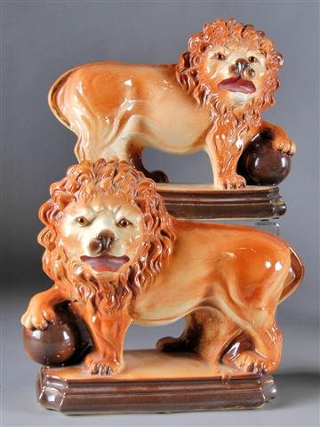 A PAIR OF STAFFORDSHIRE GLAZED EARTHENWARE FIGURES O: A PAIR OF STAFFORDSHIRE GLAZED EARTHENWARE FIGURES OF LIONS, 19th century, each modeled in a standing position with head turned and one paw resting on a sphere, raised on an eared rectangular plinth.