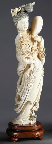 A LATE QING DYNASTY CARVED IVORY FIGURE OF QUAN YI: A LATE QING DYNASTY CARVED IVORY FIGURE OF QUAN YIN, the elegant deity modeled with right hand holding a floral bouquet and left hand holding a fan, with an elaborate avial headdress. On custom hardwo