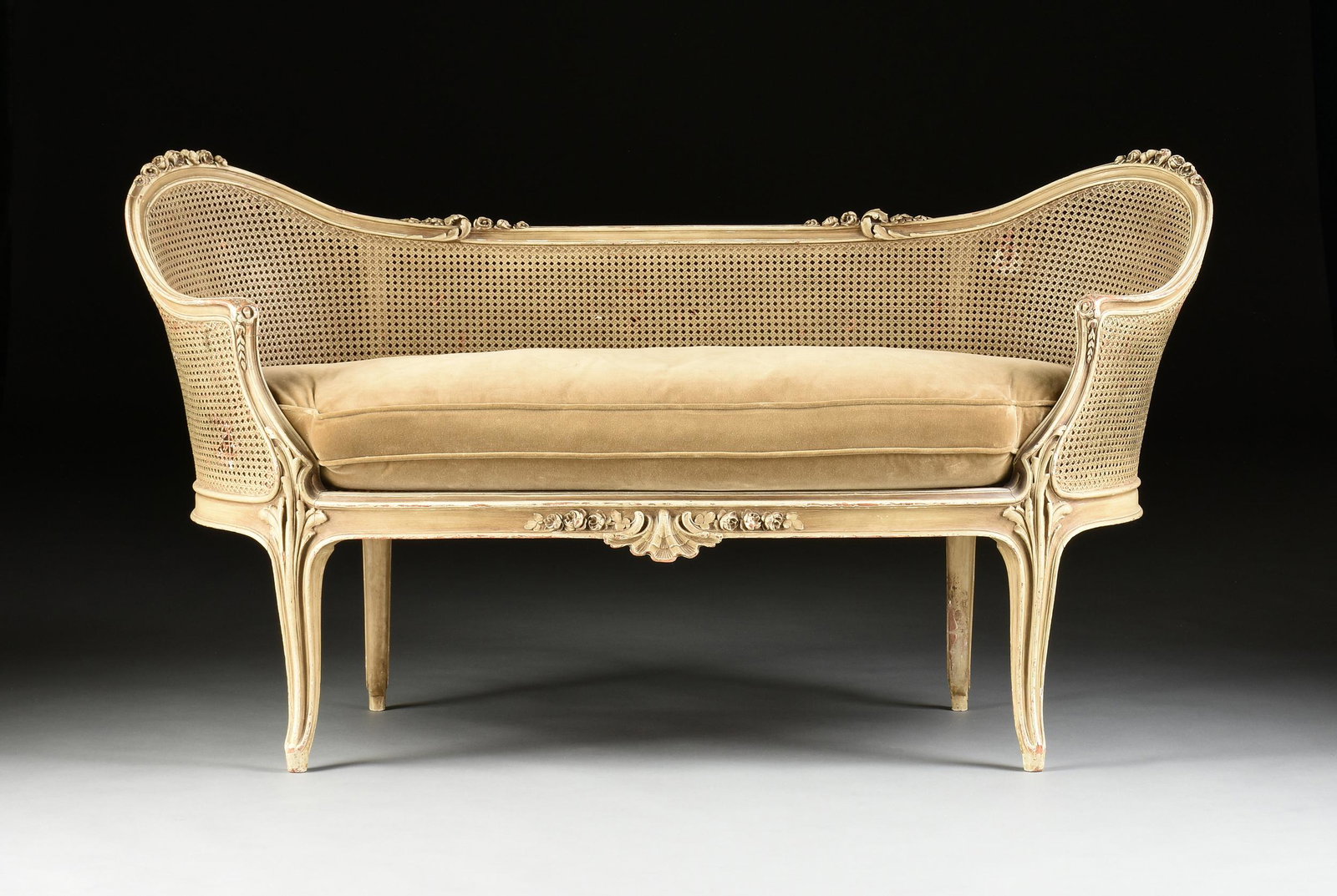 A LOUIS XV REVIVAL CANED AND PAINTED WOOD CANAPÉ, FIRST: A LOUIS XV REVIVAL CANED AND PAINTED WOOD CANAPÉ, FIRST HALF 20TH CENTURY, with a sinuous double-arched molding crest rail topped by tapering rose bloom clusters, continuing to sloped arms with flore
