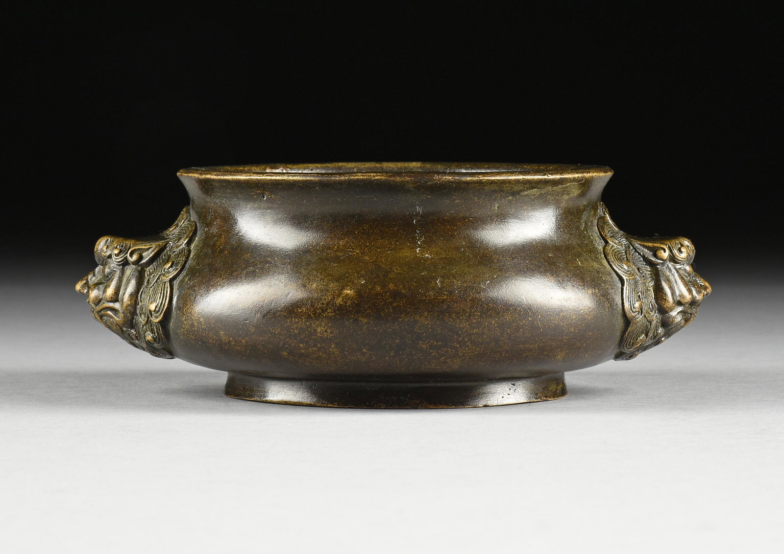 A MING DYNASTY BRONZE CENSER, XUANDE MARK, 1426-1435,: A MING DYNASTY BRONZE CENSER, XUANDE MARK, 1426-1435, the flat everted rim on a short neck flaring to a compressed cauldron form body flanked by beastly swirling hair masks with pointy ears, and curle