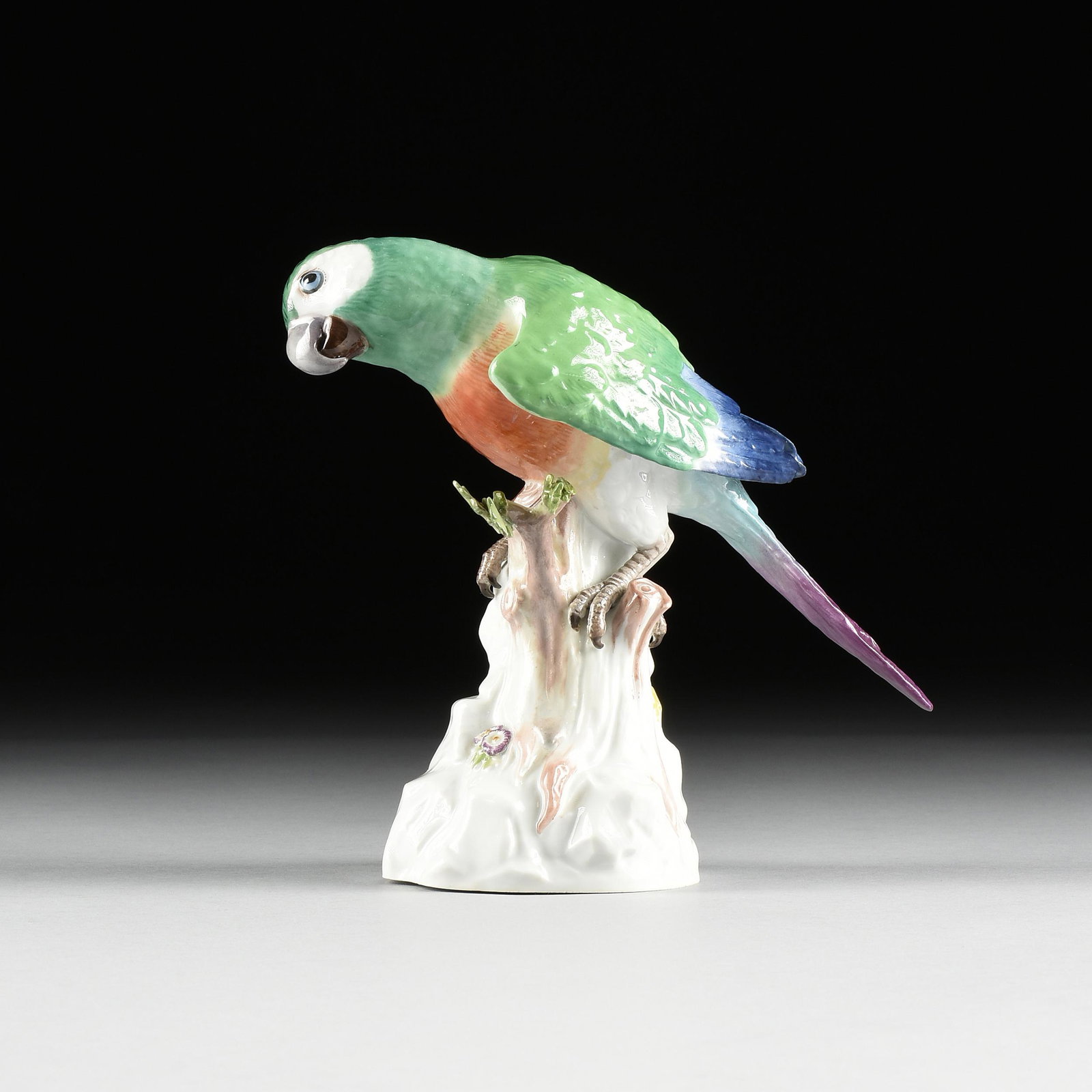 A MEISSEN PORCELAIN PARROT, MARKED, 1924-1934,: A MEISSEN PORCELAIN PARROT, MARKED, 1924-1934, painted in naturalistic shades of green, purplish-blue, and dark orange colors, modeled perched on a tree trunk on stylized rockwork with head slightly c