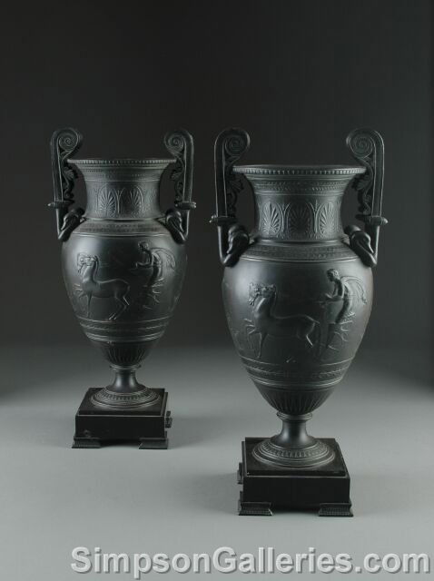 A PAIR OF NEO-GREC PATINATED METAL TWO HANDLED URNS: A PAIR OF NEO-GREC PATINATED METAL TWO HANDLED URNS, circa 1875, each of stylized amphora form and cast in shallow relief with a classically clad youth and maiden in a two horse chariot beneath a wais