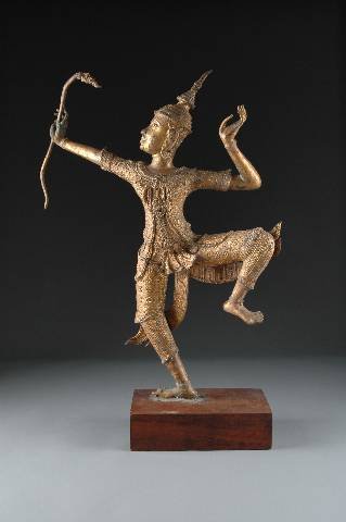 A THAI GILT METAL FIGURE OF A DANCING SNAKE CHARMER: A THAI GILT METAL FIGURE OF A DANCING SNAKE CHARMER, modeled standing on one leg with the other raised and wearing elaborately detailed attire while holding aloft a stylized serpent, raised on a recta