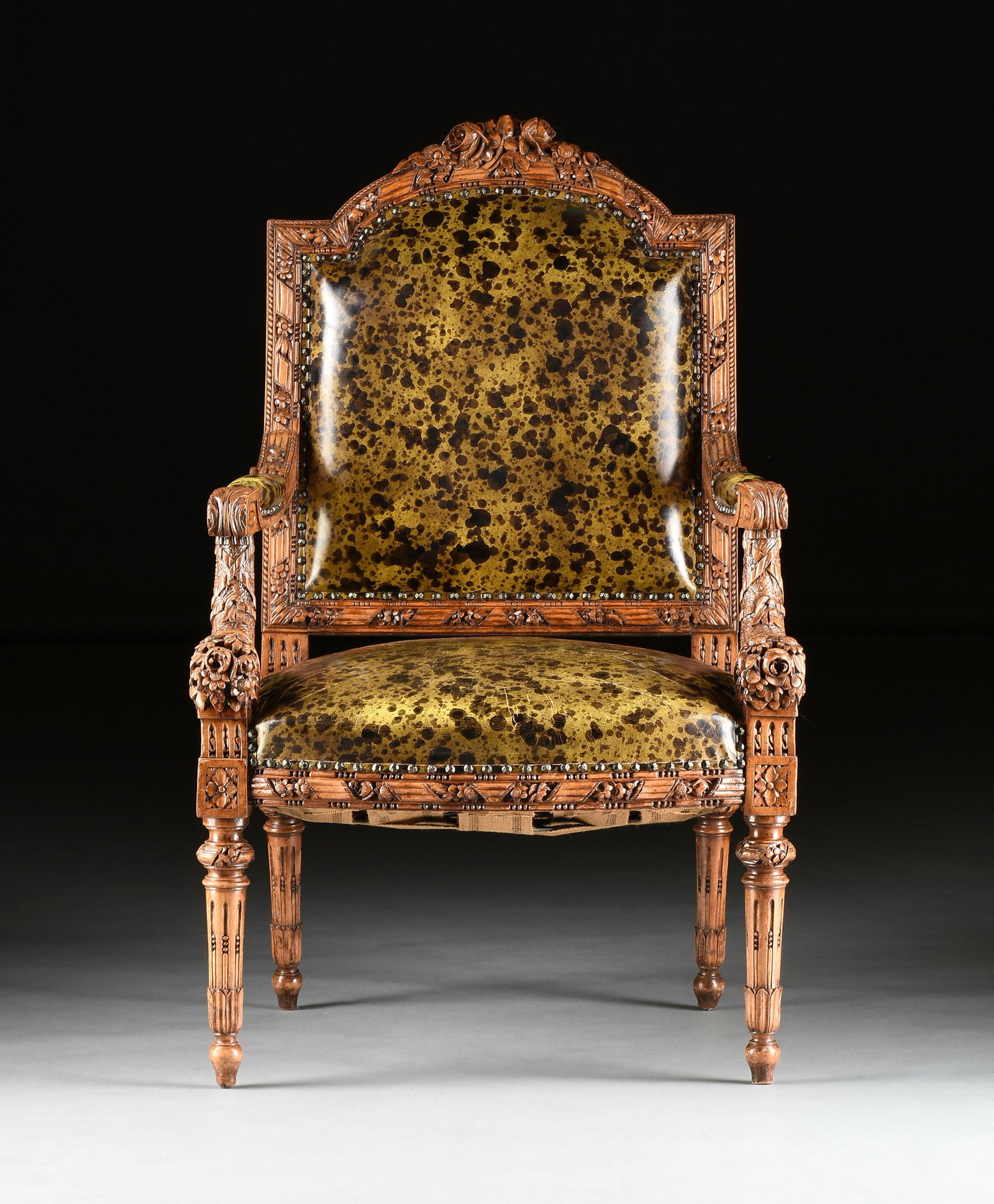 AN ITALIAN NEOCLASSICAL STYLE LEATHER UPHOLSTERED PARCEL GILT AND CARVED WOOD "CORNUCOPIA" ARMCHAIR,: AN ITALIAN NEOCLASSICAL STYLE LEATHER UPHOLSTERED PARCEL GILT AND CARVED WOOD "CORNUCOPIA" ARMCHAIR, the arched reeding crest rail topped by a floral cluster carved pendant, ending before ribbon alter