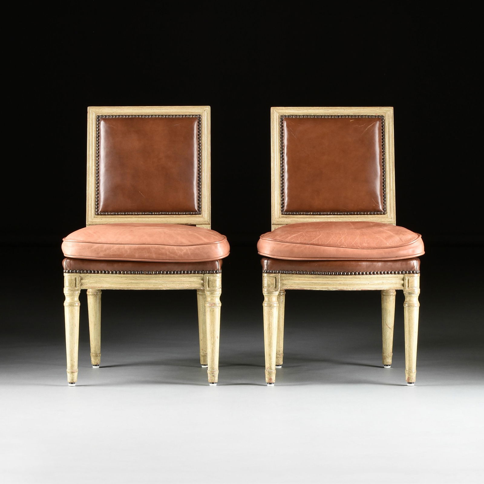 A PAIR OF LATE LOUIS XVI STYLE LEATHER UPHOLSTERED AND PAINTED WOOD CHAISES, 19TH CENTURY,: A PAIR OF LATE LOUIS XVI STYLE LEATHER UPHOLSTERED AND PAINTED WOOD CHAISES, 19TH CENTURY, each with a rectangular molded back frame above a trapezoidal seat cushion over a bow front fluted panel seat
