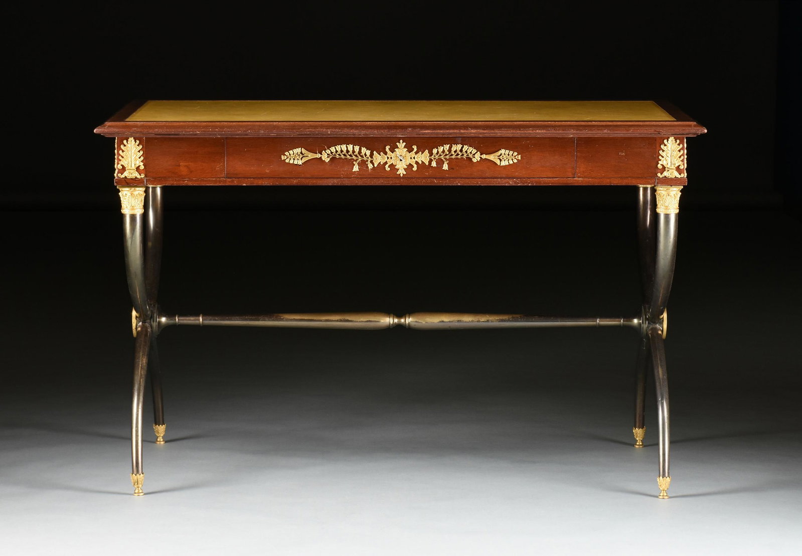 AN EMPIRE STYLE ORMOLU MOUNTED MAHOGANY AND GUN METAL BRONZE CURULE DESK, 20TH CENTURY,: AN EMPIRE STYLE ORMOLU MOUNTED MAHOGANY AND GUN METAL BRONZE CURULE DESK, 20TH CENTURY, the rectangular inset gilt tooled tan leather writing surface within conforming border and molded edge, above a 