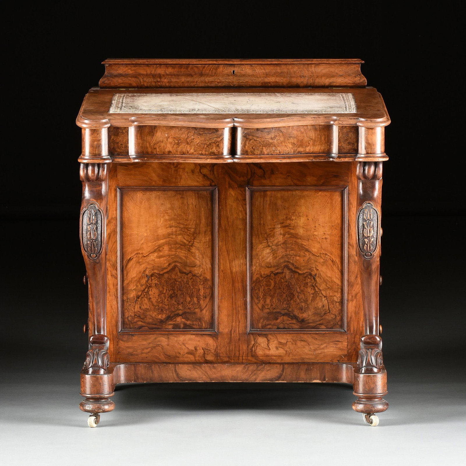 A VICTORIAN FIGURED WALNUT DAVENPORT DESK, 1840s,: A VICTORIAN FIGURED WALNUT DAVENPORT DESK, 1840s, with a hinged lidded bombé box, above a slanted rectangular top with undulating face flanked by turret corners and centering an inset gilt tooled