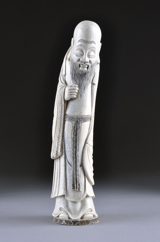 A FINE ANTIQUE CHINESE CARVED IVORY FIGURE OF AN EL: A FINE ANTIQUE CHINESE CARVED IVORY FIGURE OF AN ELDER shown standing with enlarged forehead, closed eyes, and long beard, dressed in traditional flowing robes. Signed. Height: 18"