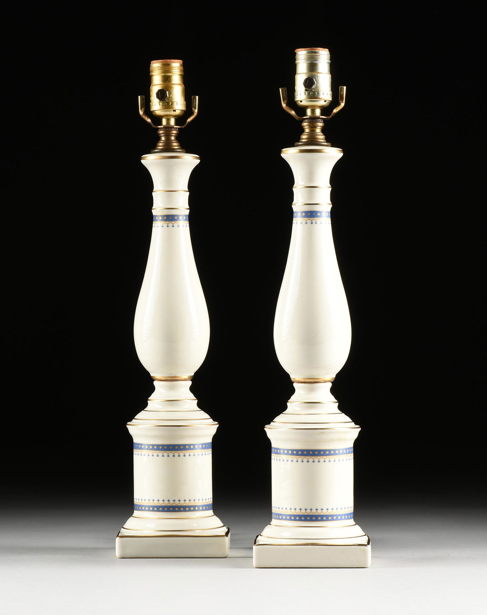 A PAIR OF FEDERAL STYLE WHITE CERAMIC TABLE LAMPS, 20TH CENTURY,: A PAIR OF FEDERAL STYLE WHITE CERAMIC TABLE LAMPS, 20TH CENTURY, of baluster form with gold star on blue banding and gilt line decoration, wired. Height: 28 3/4'' Width: 4 1/4'' Depth: 4 1/4''