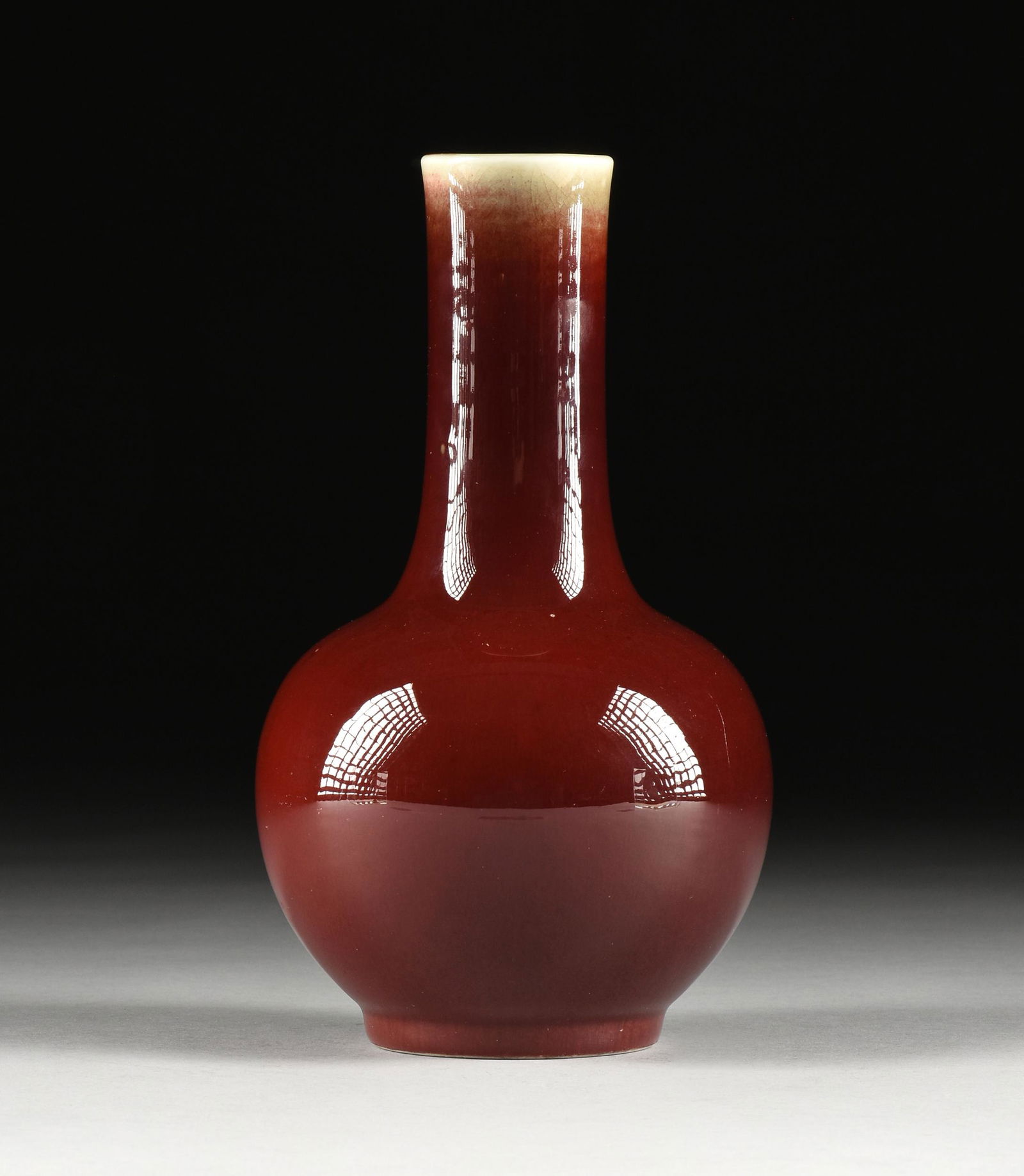 A CHINESE SANG DE BOEUF GLAZED BOTTLE FORM PORCELAIN VASE, EARLY 20TH CENTURY,: A CHINESE SANG DE BOEUF GLAZED BOTTLE FORM PORCELAIN VASE, EARLY 20TH CENTURY, the long cylindrical neck flaring to a bulbous body with white glazed rim continuing to interior body and thinning to oxb