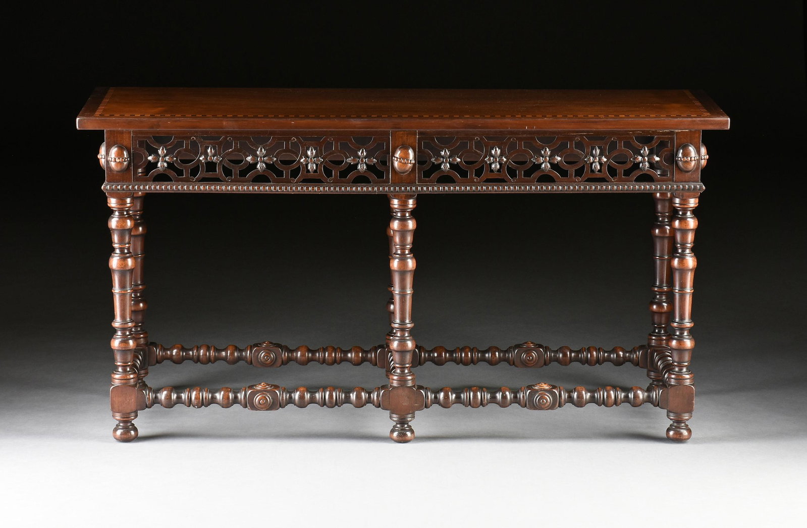 A JACOBEAN STYLE CARVED WALNUT CONSOLE TABLE, LATE 20TH CENTURY,: A JACOBEAN STYLE CARVED WALNUT CONSOLE TABLE, LATE 20TH CENTURY, the rectangular top with maple and mahogany squares banded border above a pierced fretwork frieze, on turned bun and cylinder legs endi