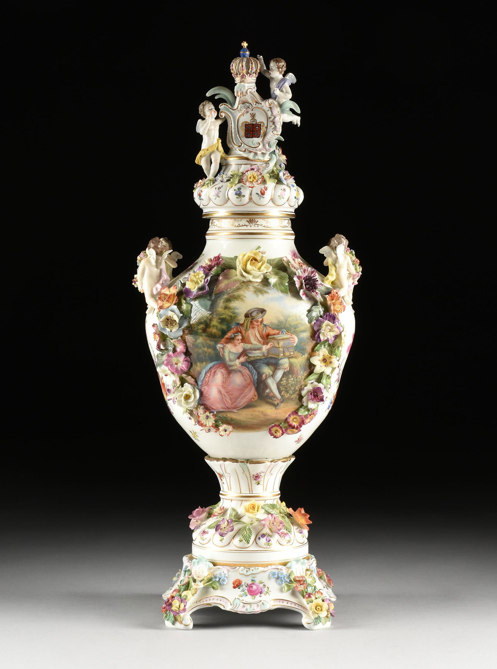 A CARL THIEME FLORAL ENCRUSTED AND FIGURAL PORCELAIN LIDDED VASE ON STAND, MARKED, DRESDEN, GERMANY,: A CARL THIEME FLORAL ENCRUSTED AND FIGURAL PORCELAIN LIDDED VASE ON STAND, MARKED, DRESDEN, GERMANY, EARLY 20TH CENTURY, the shaped circular lid surmounted by a cross topped crown, on a cartouche fram