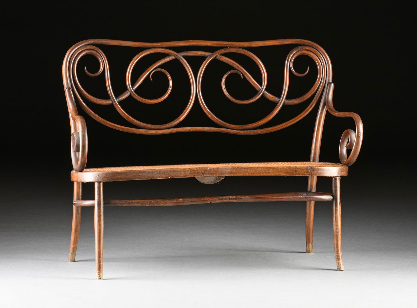 A CZECH D.G. FISCHEL CANED AND BENTWOOD SETTEE, PARTIALLY LABELED, NIEMES, BOHEMIA, EARLY 20TH: A CZECH D.G. FISCHEL CANED AND BENTWOOD SETTEE, PARTIALLY LABELED, NIEMES, BOHEMIA, EARLY 20TH CENTURY, the undulating elongated oval framed back enclosing swirling scrolls and issuing curling arms, e