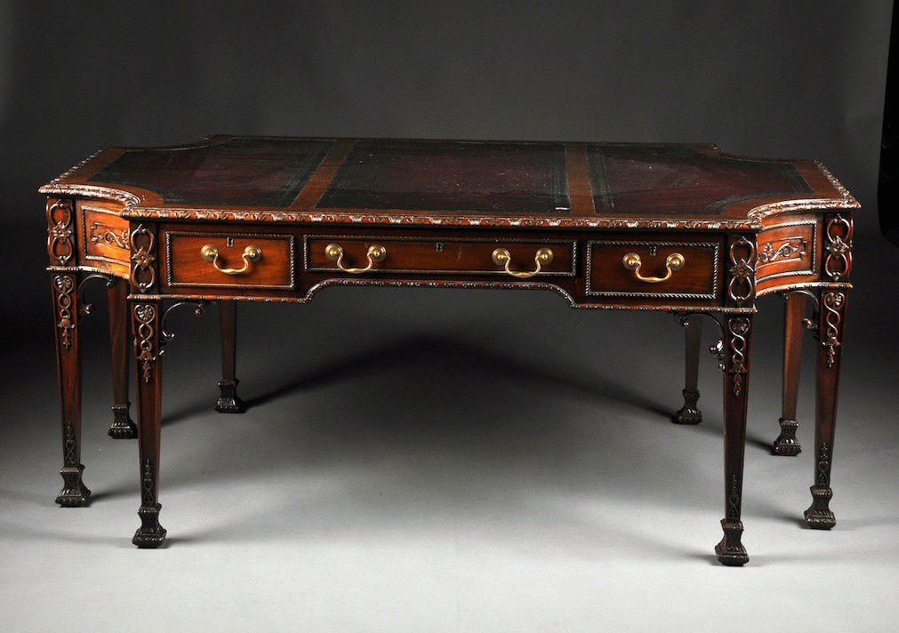 A GEORGE III MAHOGANY PARTNERS DESK in the style of: A GEORGE III MAHOGANY PARTNERS DESK in the style of Thomas Chippendale, the top with incurvate corners and tooled leather insets surrounded by a shell patterned frieze, each oblong side with 3 rope tw
