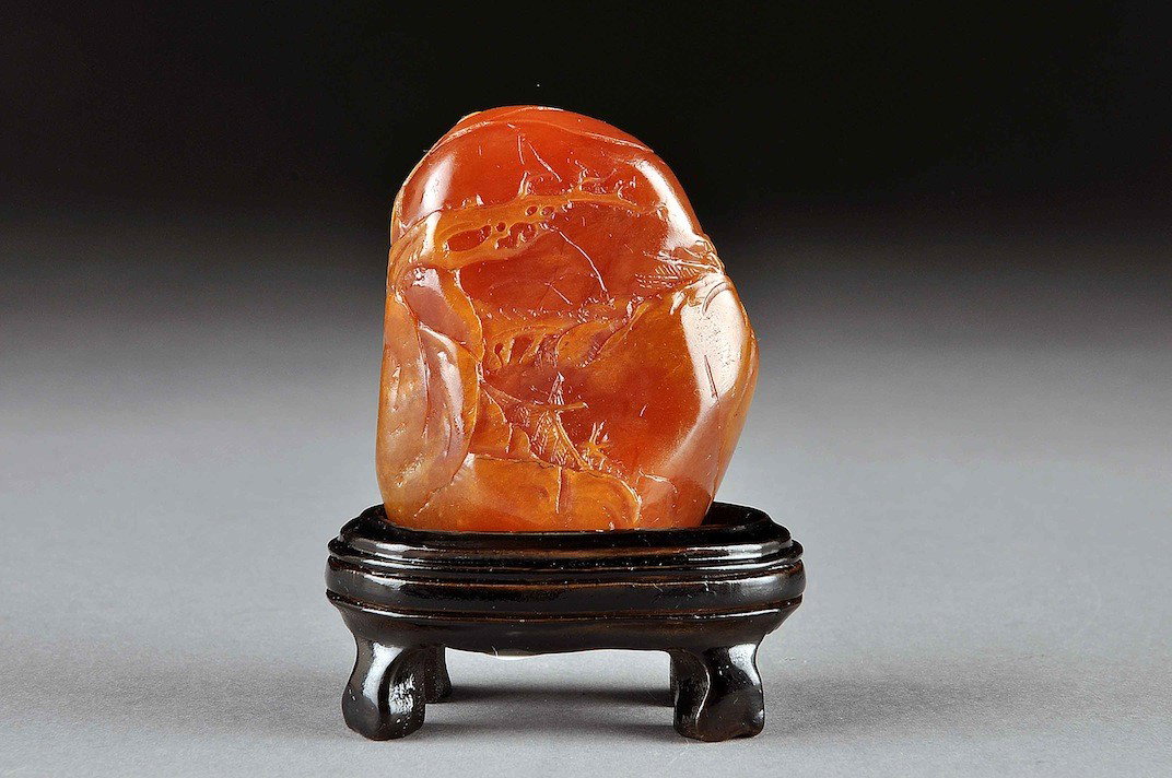 A CHINESE SHOUSHAN SOAPSTONE TIANHUANG CARVING, 20: A CHINESE SHOUSHAN SOAPSTONE TIANHUANG CARVING, 20TH CENTURY, of natural boulder form and nicely detailed in shallow relief with two elders in a junk moored amidst a rocky waterside setting beneath an