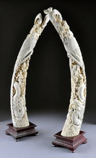 A PAIR OF INTRICATELY CARVED VINTAGE CHINESE PEACO: A PAIR OF INTRICATELY CARVED VINTAGE CHINESE PEACOCK AND DRAGON IVORY TUSKS, THIRD QUARTER 20TH CENTURY, each reticulated tusk surmounted by a figure of Guanyin seated in the royal ease or Rajalilasan