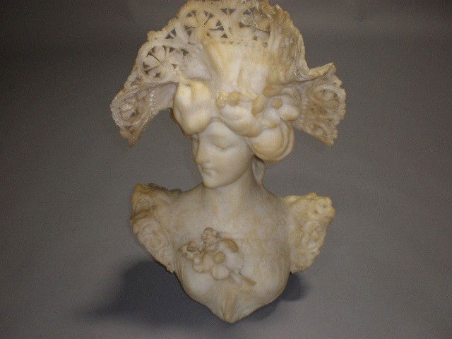 A CARVED ALABASTER BUST OF A FEMALE: A CARVED ALABASTER BUST OF A FEMALE wearing a lace bonnet with flowers and a lace trimmed dress. Some losses. H: 25".