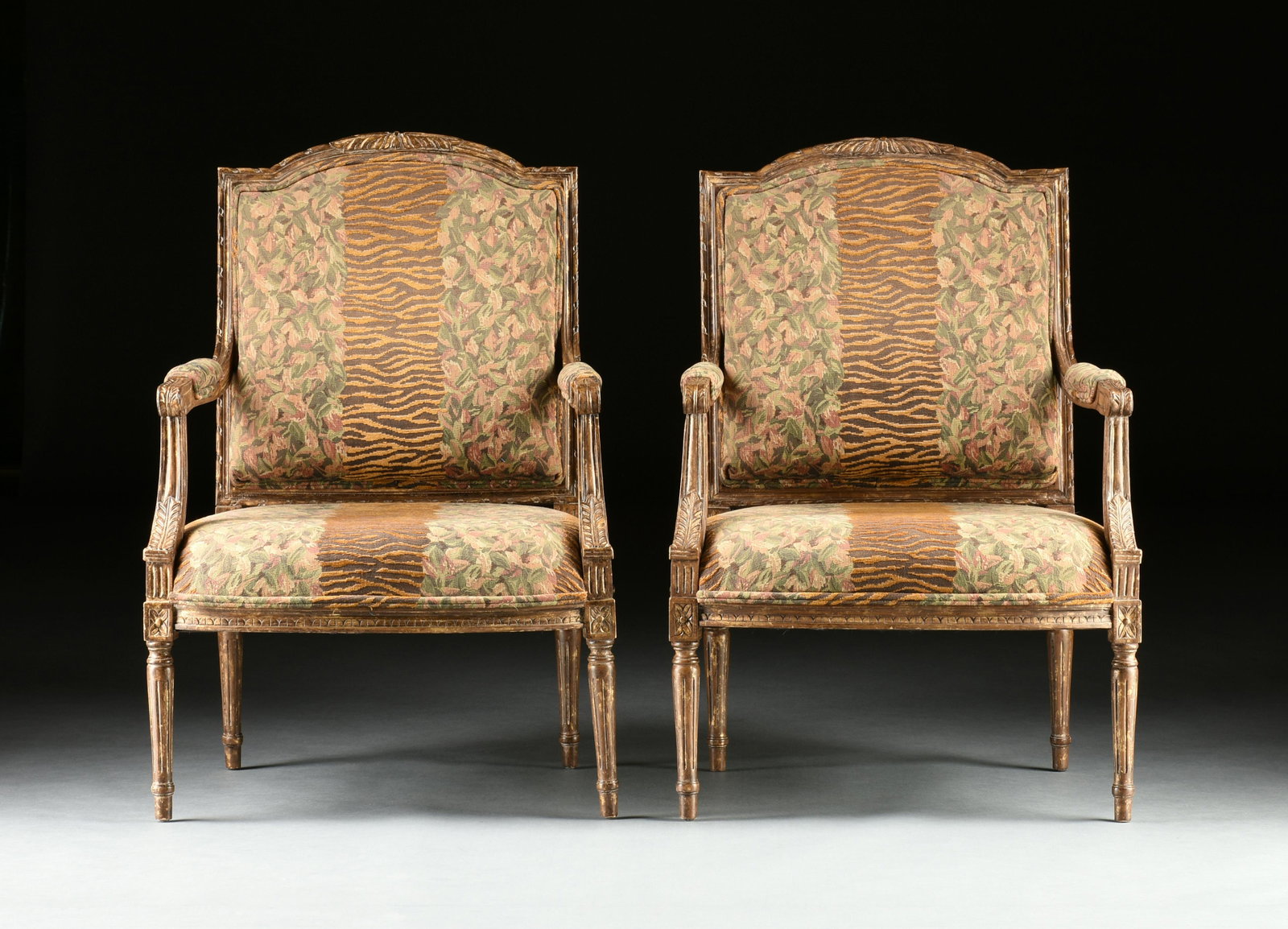 A PAIR OF LOUIS XVI STYLE PARCEL GILT FAUTEUIL ARMCHAIRS, 20TH CENTURY,: A PAIR OF LOUIS XVI STYLE PARCEL GILT FAUTEUIL ARMCHAIRS, 20TH CENTURY, carved and upholstered with floral and tiger stripe pattern. Height: 40" Width: 27 1/2" Depth: 22"