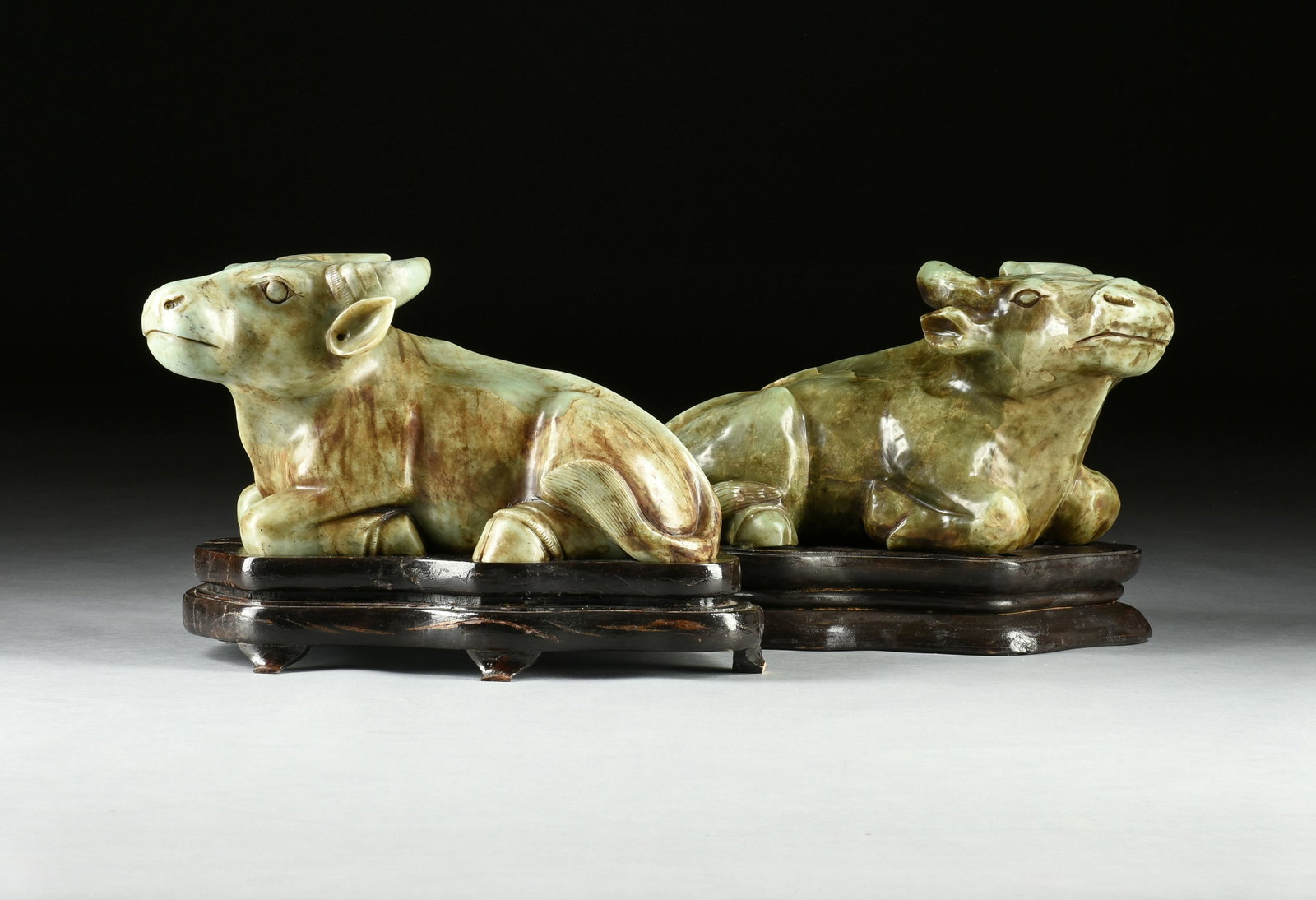 TWO MING DYNASTY STYLE JADE WATER BUFFALO, PROBABLY QING DYNASTY,: TWO MING DYNASTY STYLE JADE WATER BUFFALO, PROBABLY QING DYNASTY, the mottled celadon green nephrite jade, carved with naturalism, is a recumbent ox with swept back horns, a spiraling auspicious urna 