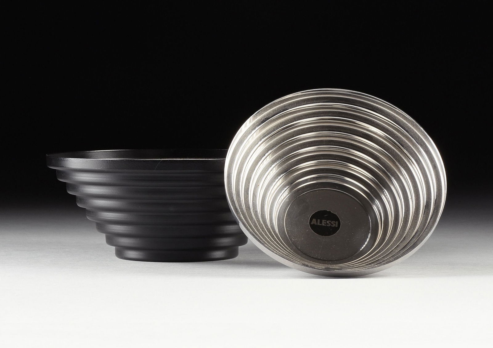 TWO STEEL "MAYA" BOWLS BY ALESSI, ITALIAN, CIRCA 1970s,: TWO STEEL "MAYA" BOWLS BY ALESSI, ITALIAN, CIRCA 1970s, designed by Giulio Confalonieri, each with stepped sides, one with a black epoxy resin finish for cooking, height: 4", diameter: 9 3/4", one sta