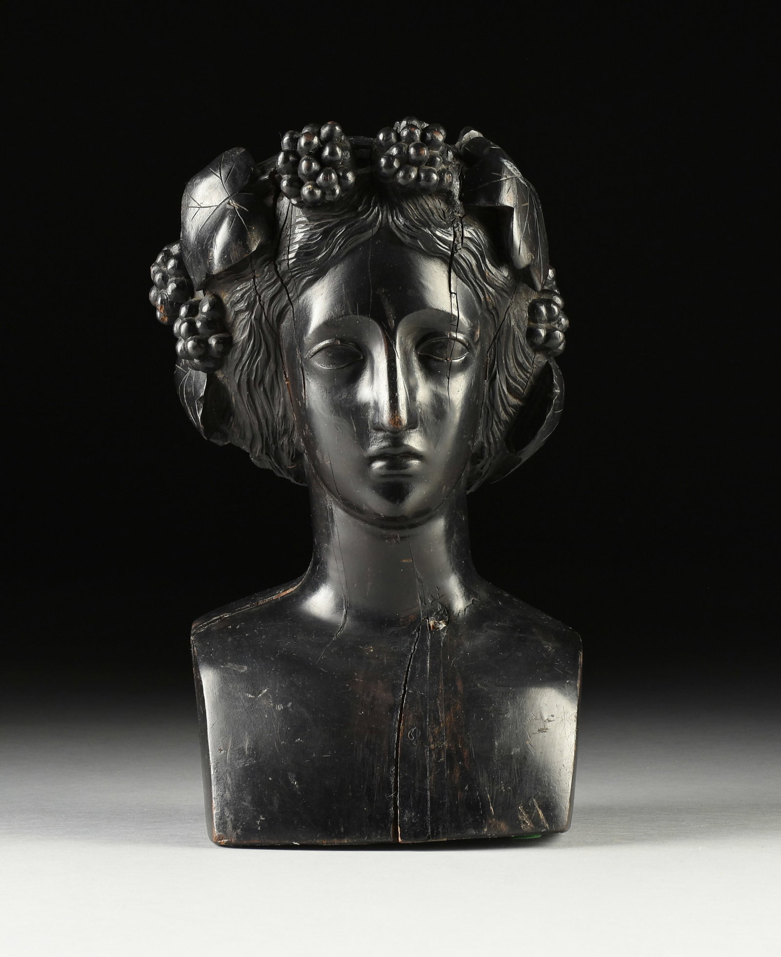A NEOCLASSICAL REVIVAL EBONIZED WOOD BUST OF, "Dionysus," PROBABLY FRENCH, 18TH/19TH CENTURY,: A NEOCLASSICAL REVIVAL EBONIZED WOOD BUST OF, "Dionysus," PROBABLY FRENCH, 18TH/19TH CENTURY, the waving hair parted at center is tucked at back and fitted with a diadem of full grape bunches and wide