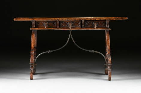 A SPANISH BAROQUE WALNUT AND WROUGHT IRON TRESTLE LIBRARY TABLE, 18TH CENTURY,: A SPANISH BAROQUE WALNUT AND WROUGHT IRON TRESTLE LIBRARY TABLE, 18TH CENTURY, the thick rectangular single plank top with curled grain, on a three-drawer frieze with rhombus lozenge carved faces and