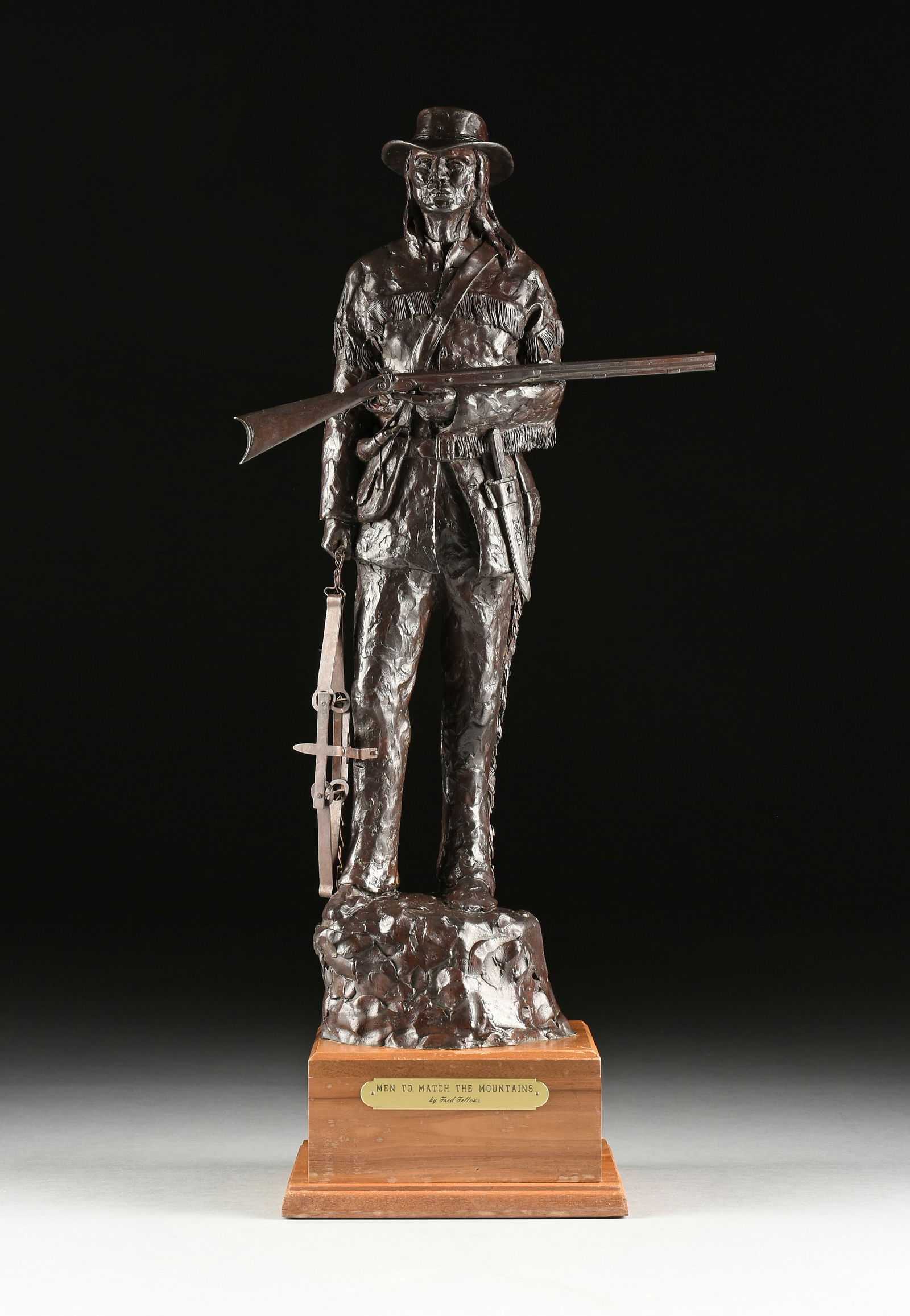 FRED FELLOWS, (American b. 1934) A BRONZE SCULPTURE, "Men to Match the Mountains," 20TH CENTURY,: FRED FELLOWS, (American b. 1934) A BRONZE SCULPTURE, "Men to Match the Mountains," 20TH CENTURY, the standing patinated bronze figure cast holding a rifle and animal trap, signed and incised in the br