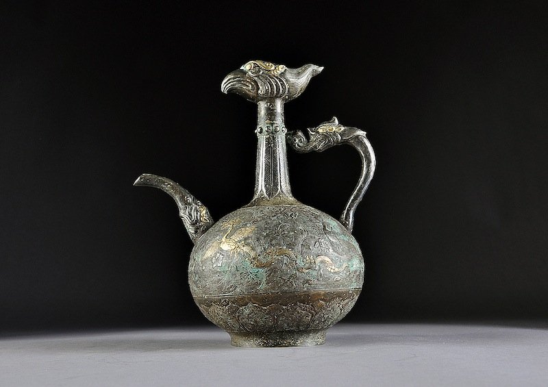 A RARE CHINESE "PHOENIX HEAD" PARCEL GILT REPOUSSƒ : A RARE CHINESE "PHOENIX HEAD" PARCEL GILT REPOUSSƒ AND ENGRAVED SILVER ALLOY EWER, POSSIBLY TANG DYNASTY, (AD 618 - 907), the bottle form body centering meandering blossoming foliate vines on a fine 