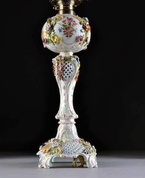 A DRESDEN FLORAL ENCRUSTED AND POLYCHROME PAINTED : A DRESDEN FLORAL ENCRUSTED AND POLYCHROME PAINTED OIL LAMP BY THE CARL THIEME FACTORY, EARLY 20TH CENTURY, in the Rococo taste with the reticulated stem molded with stylized leaf details continuing to