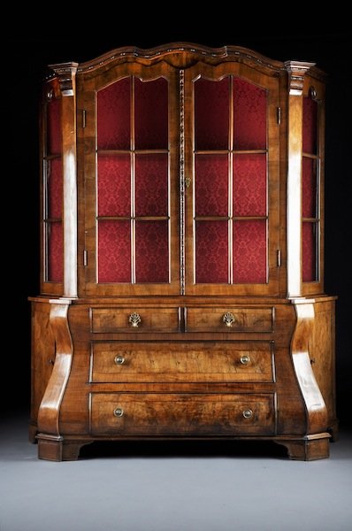 A CONTINENTAL CARVED WALNUT VITRINE CABINET, POSSI: A CONTINENTAL CARVED WALNUT VITRINE CABINET, POSSIBLY ITALIAN, SECOND HALF 20TH CENTURY, the undulating molded cornice above conforming glazed doors opening to a red silk damask lined fixed shelf inte