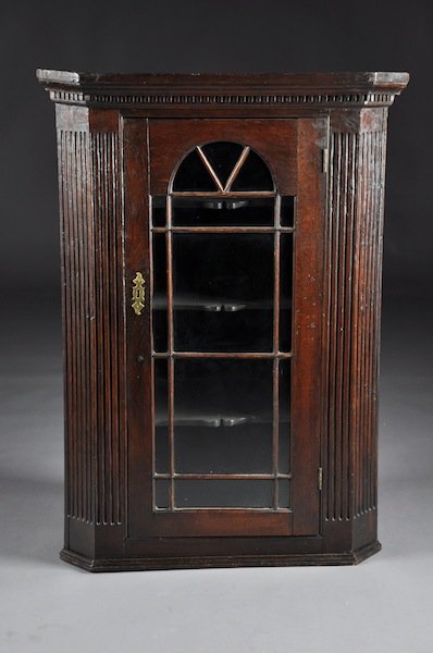 A GEORGE III CARVED OAK CORNER CABINET, LATE 18TH/: A GEORGE III CARVED OAK CORNER CABINET, LATE 18TH/EARLY 19TH CENTURY, the molded and dentilated cornice above a hinged glazed door with arched mullions opening to fixed shelves with shaped borders and