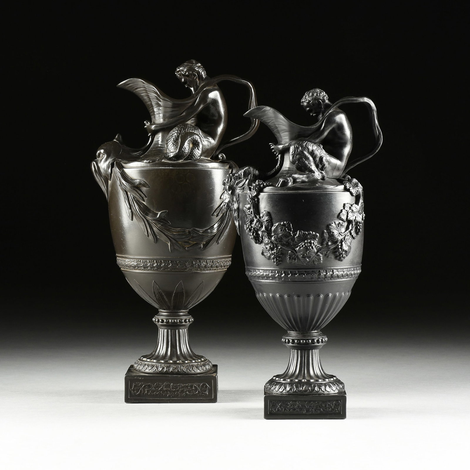TWO WEDGWOOD BLACK BASALT EWERS EMBLEMATIC OF WATER AND WINE, SACRED TO NEPTUNE AND BACCHUS, AFTER J: TWO WEDGWOOD BLACK BASALT EWERS EMBLEMATIC OF WATER AND WINE, SACRED TO NEPTUNE AND BACCHUS, AFTER JOHN FLAXMAN AND SIGISBERT FRANÇOIS MICHEL, IMPRESSED MARKS, ENGLISH, 19TH AND EARLY 20TH CENTUR