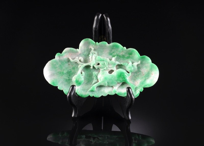 AN ANTIQUE CHINESE CARVED APPLE GREEN JADEITE DISH,: AN ANTIQUE CHINESE CARVED APPLE GREEN JADEITE DISH, QING DYNASTY, of lotus leaf form and detailed in deep relief with a striding mythical Qi-lin clutching a lotus bud stem in its snarling jaws enclose