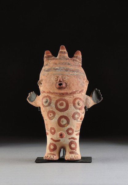 A PRE-COLUMBIAN CHANCAY CUCHIMILCO POTTERY MALE FI: A PRE-COLUMBIAN CHANCAY CUCHIMILCO POTTERY MALE FIGURE, NORTH COAST PERU, C. 1100 A.D., on tubular legs with short arms raised and palms open the body painted with circular tattoos wearing a spiked he
