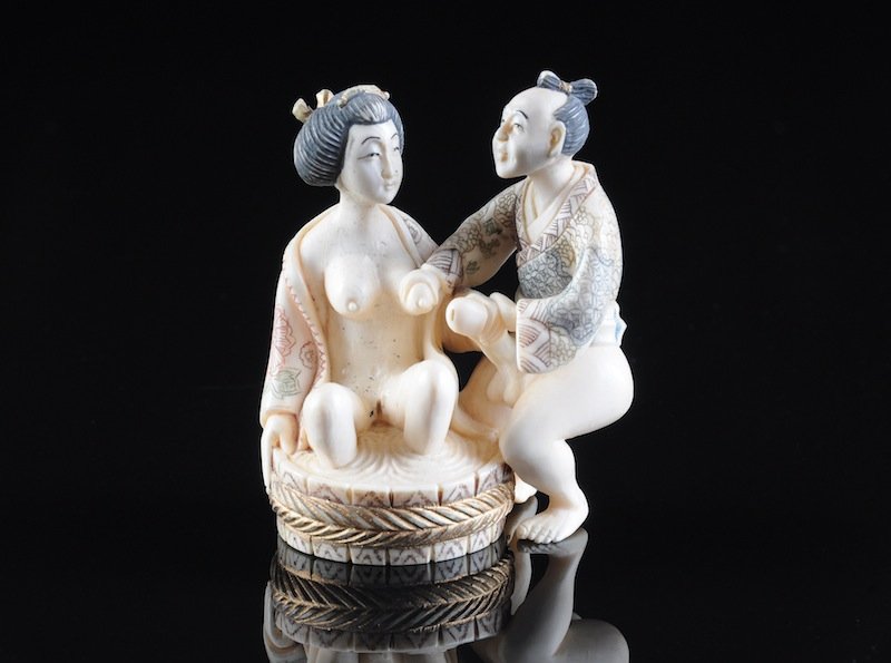 A JAPANESE POLYCHROME CARVED IVORY EROTIC NETSUKE,: A JAPANESE POLYCHROME CARVED IVORY EROTIC NETSUKE, SIGNED, 20TH CENTURY, modeled as a scantily clad maiden seated in a tub of water being assisted by her husband, underside centering two character art