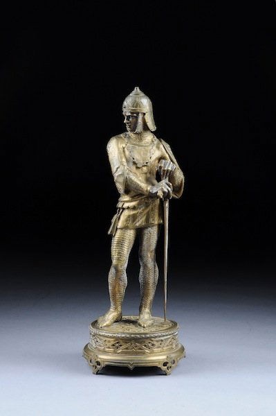 A CONTINENTAL GILT BRONZE FIGURE OF A MEDIEVAL KNI: A CONTINENTAL GILT BRONZE FIGURE OF A MEDIEVAL KNIGHT, PROBABLY FRENCH, LATE 19TH/EARLY 20TH CENTURY, modeled in a standing position holding a large sheathed sword while wearing a helmet above a fierc