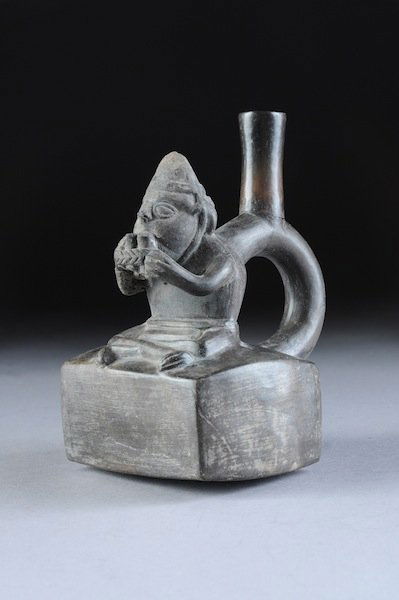 A PRE-COLUMBIAN CHIMÚ CULTURE VESSEL, CIRCA 1200 A: A PRE-COLUMBIAN CHIMÚ CULTURE VESSEL, CIRCA 1200 A.D., with a warrior seated playing a flute with stirrup handle. Height: 7". NOTE: The Chimú were the residents of Chimor, with its capital at the ci