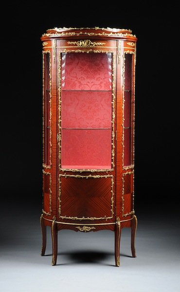 A LOUIS XV STYLE GILT METAL MOUNTED CARVED WOOD VI: A LOUIS XV STYLE GILT METAL MOUNTED CARVED WOOD VITRINE, MODERN, of demilune shape with foliate cast encadrements centering conforming glazed panels enclosing a crimson damask lined interior, raised o