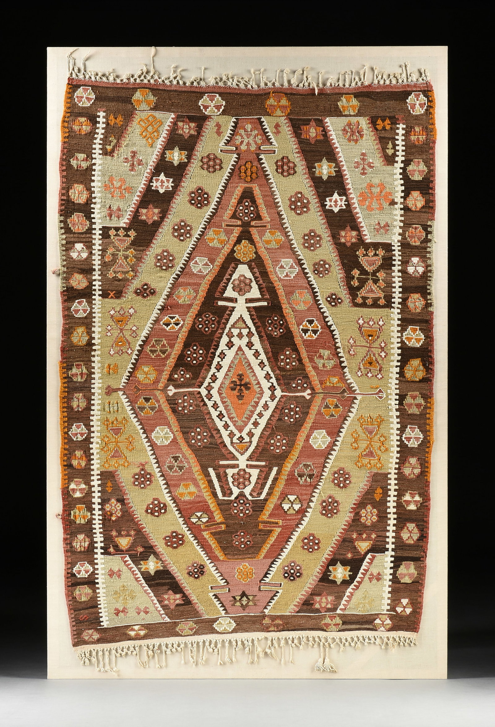 A TRIBAL ANATOLIAN KILIM RUG, TURKEY, 19TH CENTURY: A TRIBAL ANATOLIAN KILIM RUG, TURKEY, 19TH CENTURY, naturally dyed wool in brown, pistachio, red, orange, and cream with stars, flowers, and pinwheels with central diamond motif; 84" x 53 1/2", linen-