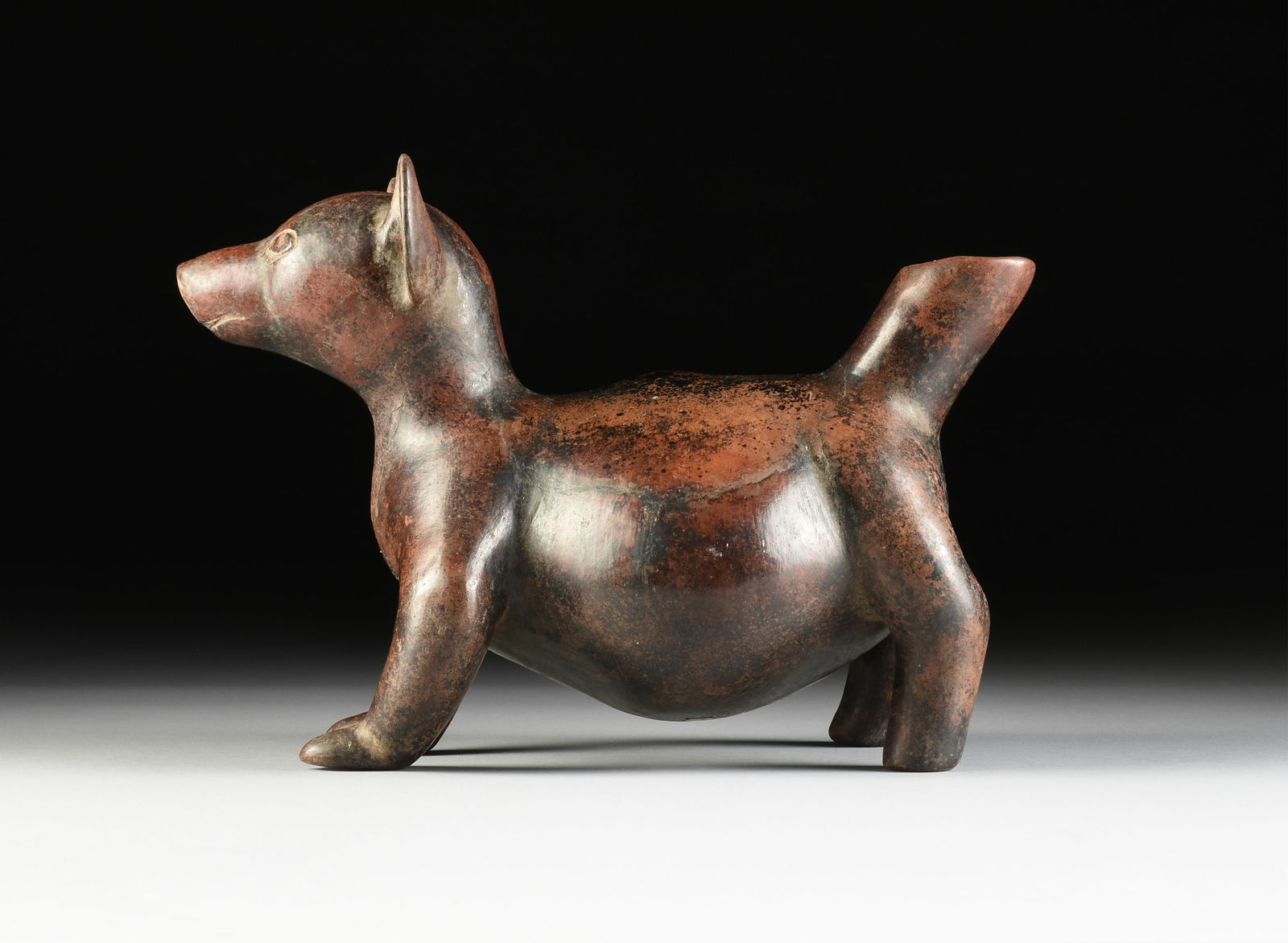 A COLIMA REDWARE POTTERY TECHICHI DOG EFFIGY, MEXICO, CIRCA AD 800-1200: A COLIMA REDWARE POTTERY TECHICHI DOG EFFIGY, MEXICO, CIRCA AD 800-1200, fired clay in the form of a good dog with wide shoulders, a corpulent belly, a hollow tail, and perked ears. Height: 10" Width: